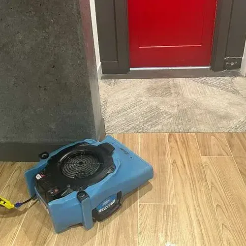 Air mover drying a wood-look tile floor beside an open doorway during a dry-out