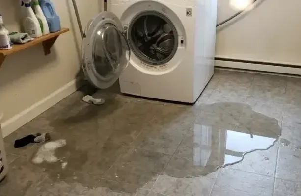 Water pooled across a laundry room floor in front of a washing machine