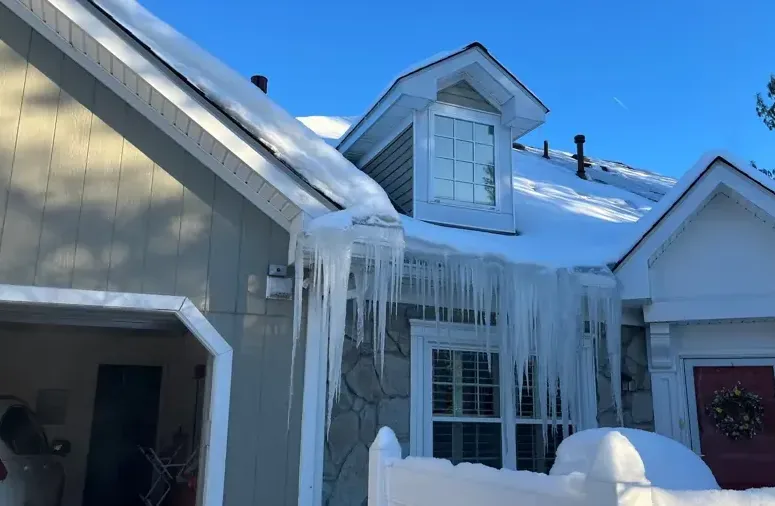 A thick ice dam with icicles hanging from the snow-covered eaves of a house